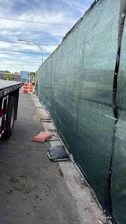 Tall temporary fence panels with green windscreen on an active construction site